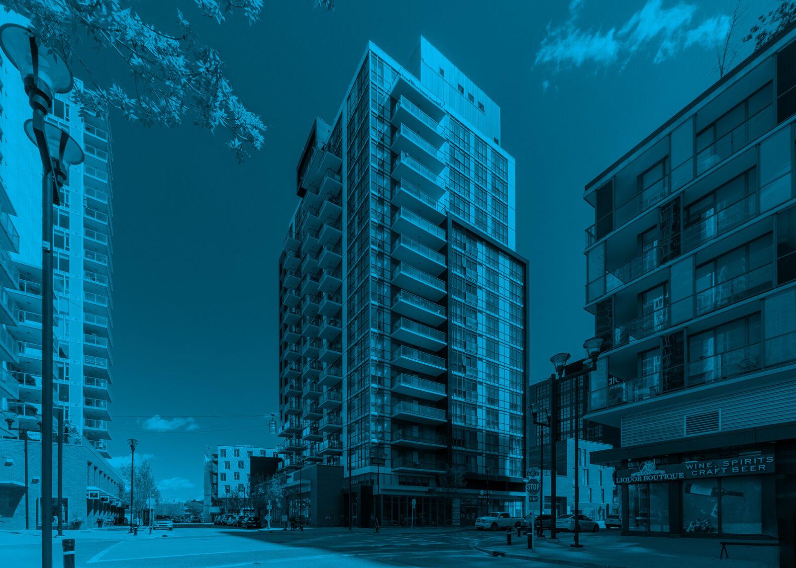 Modern high-rise residential building with glass façade and balconies on a city corner, surrounded by urban streets and neighboring condos, viewed under a clear sky with blue overlay.