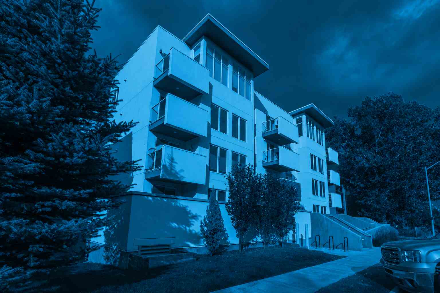 Blue-toned modern condominium building with private balconies and landscaped surroundings, illustrating housing options and considerations when comparing renting vs buying a condo in an urban residential community.